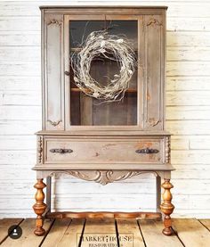 an old china cabinet with a wreath on it's door and some wood legs