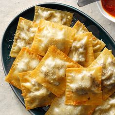 some ravioli with cheese and sauce on a blue plate next to a bowl of ketchup