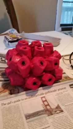 a pile of red flowers sitting on top of a table next to a newspaper and glasses