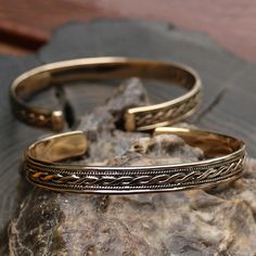 two gold bracelets sitting on top of a rock next to a piece of wood