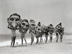 five people with masks on their heads walking along the beach in front of the ocean