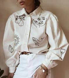 a woman wearing a white shirt with drawings on it