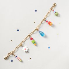 a gold chain bracelet with colorful beads and charms hanging from it's sides on a white surface