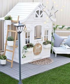 a white doll house with plants and lights on the roof, next to a light pole