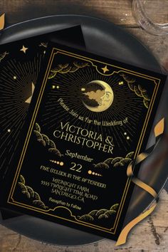 a black and gold wedding card with the moon in the sky above it on a plate