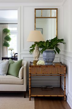 a living room with a couch, mirror and plant on the end table in front of it