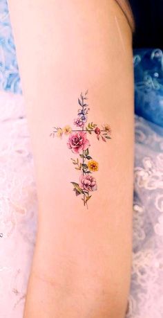 a cross tattoo with flowers on the side of her leg and behind her is an image of a woman's legs