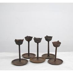 five metal candlesticks are lined up against a white background, with one candle holder in the middle