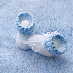 two crocheted baby booties sitting on top of a blue blanket with a white ribbon