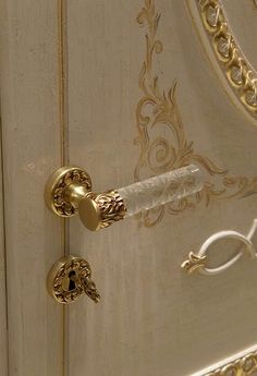 an ornate door handle on a white and gold painted cabinet