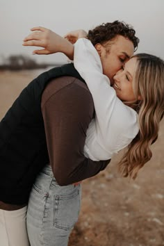 two women hugging each other in the middle of an open field with dirt and grass