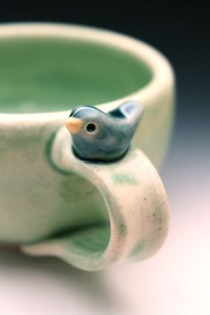 a blue bird figurine sitting on top of a white cup with green rim