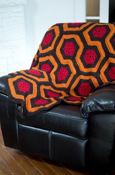 a black leather chair with an orange and red blanket on it