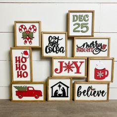 a number of framed christmas signs on a wooden table next to a white brick wall