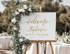 a welcome sign with greenery and white flowers is on an easel at a wedding reception