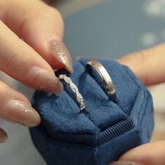 a woman holding onto a wedding ring in a blue velvet box with her fingers on it