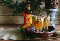 two glasses filled with drinks sitting on top of a wooden tray next to pine cones