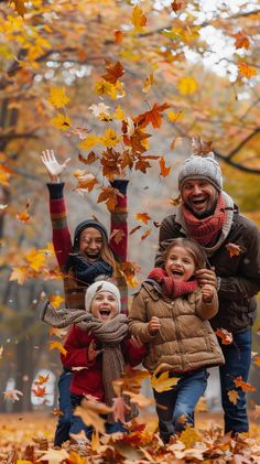 two adults and two children playing with leaves in an autumn park, one holding his hands up to the sky