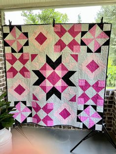 a pink and black quilt hanging on a brick wall next to a potted plant