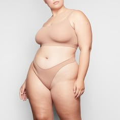 a woman wearing a nude colored bikinisuit with her hands on her hips, standing in front of a white background