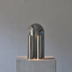 two silver vases sitting on top of a cement block in front of a gray wall