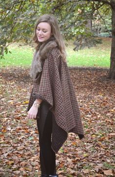 a woman standing in the leaves wearing a cape