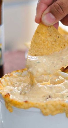 a hand dipping a tortilla chip into a white bowl filled with cheese dip