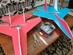 two paper airplanes sitting on top of a wooden table next to scissors and pliers