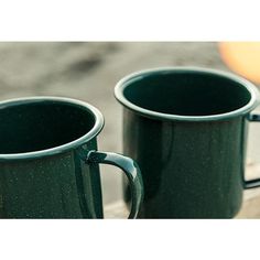 two green mugs sitting next to each other on a wooden table with an orange in the background