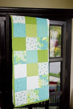 a green and white quilt hanging from a book shelf