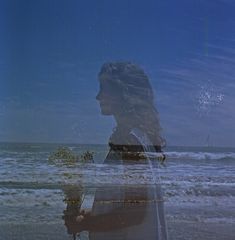 a woman standing in front of the ocean holding flowers