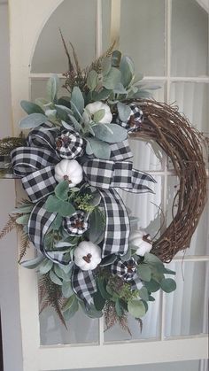 a wreath with white pumpkins and greenery on it