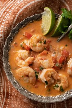 a bowl filled with shrimp and garnish on top of a table next to a lime wedge