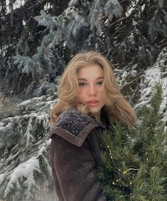 a woman is standing in the snow holding a christmas tree and looking at the camera