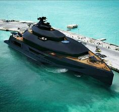 a large black boat in the water next to a dock with people walking on it