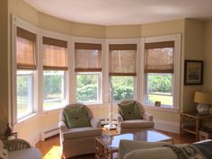 a living room filled with furniture and windows covered in roman blind shades on top of them