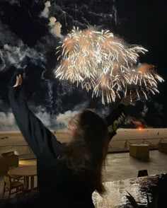 a woman is holding her arms up in the air as fireworks go off