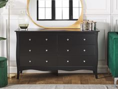 a black dresser and mirror in a room with white walls, wooden floors and green furniture