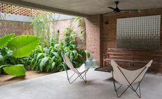 two chairs sitting on top of a cement floor next to a wooden bench and green plants