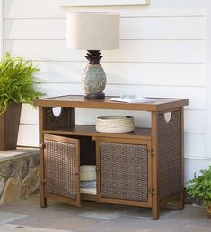 a table with baskets and a lamp on it in front of a white house next to a potted plant