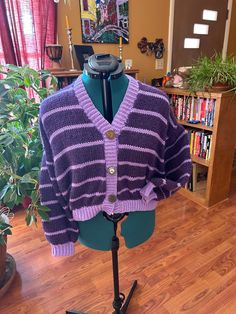 a purple and black sweater sitting on top of a mannequin next to a potted plant