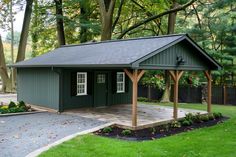 a green shed with a black roof in the middle of a driveway and lots of trees