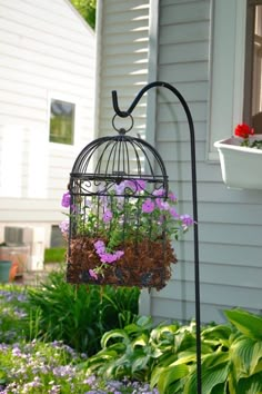 a birdcage with flowers hanging from it's side in front of a house