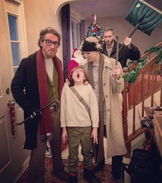 two adults and a child standing in front of a staircase with christmas decorations on it