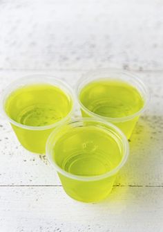 four plastic cups filled with green liquid sitting on top of a white wooden table next to each other