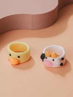 two rubber ducks sitting next to each other on top of a pink surface with an oval shaped object in the background