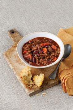 a bowl of chili with bread on a cutting board