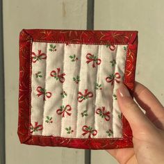 a hand holding a small red and white quilted case with bows on the front