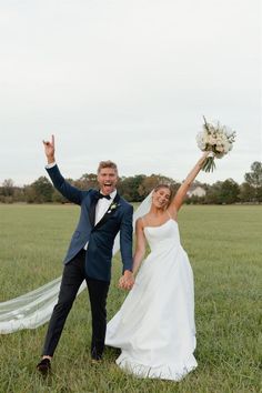 a newly married couple holding hands and posing for a photo in the grass with their arms up