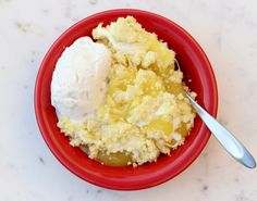 a red bowl filled with ice cream on top of a white counter next to a spoon